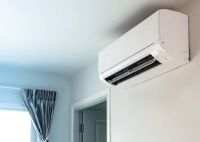 White wall-mounted air conditioner above a doorway, near a window with a gray curtain.