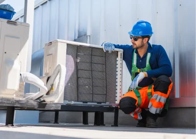 Worker in safety gear inspects an outdoor air conditioning unit on a rooftop.