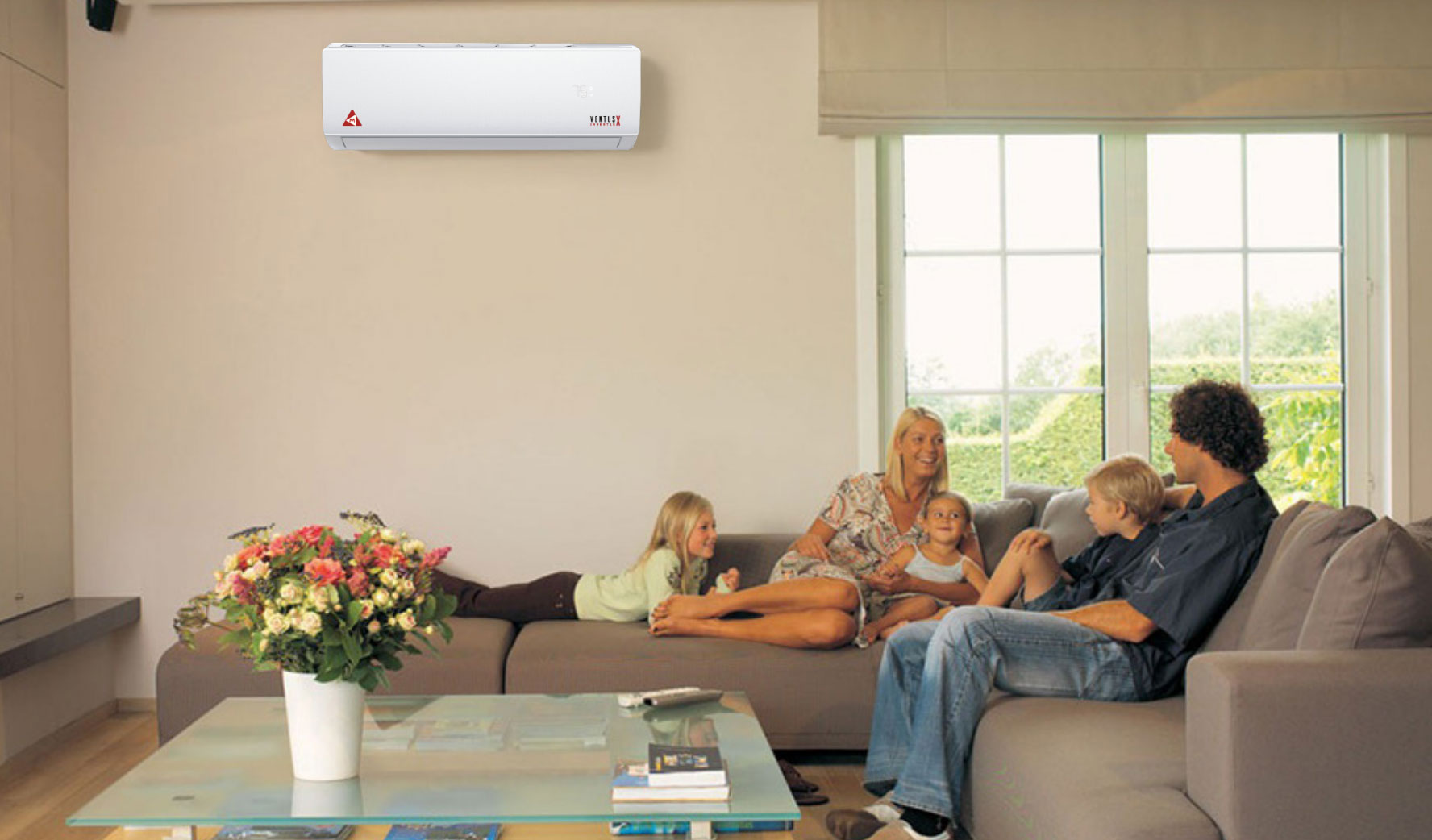 Family of four relaxes on a sofa in a bright living room with flowers and an air conditioner on the wall.