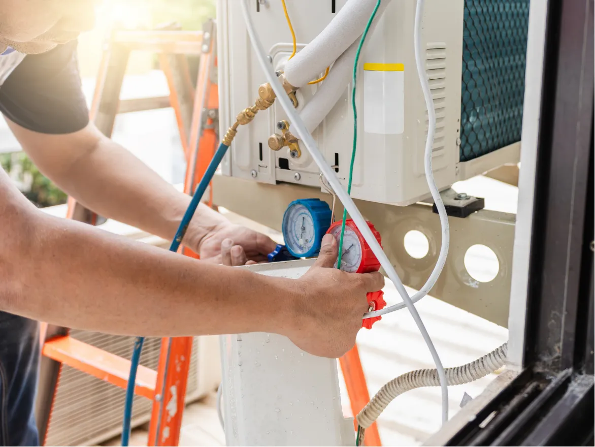 Technician adjusting pressure gauges on an air conditioning unit, with tools and wires visible.