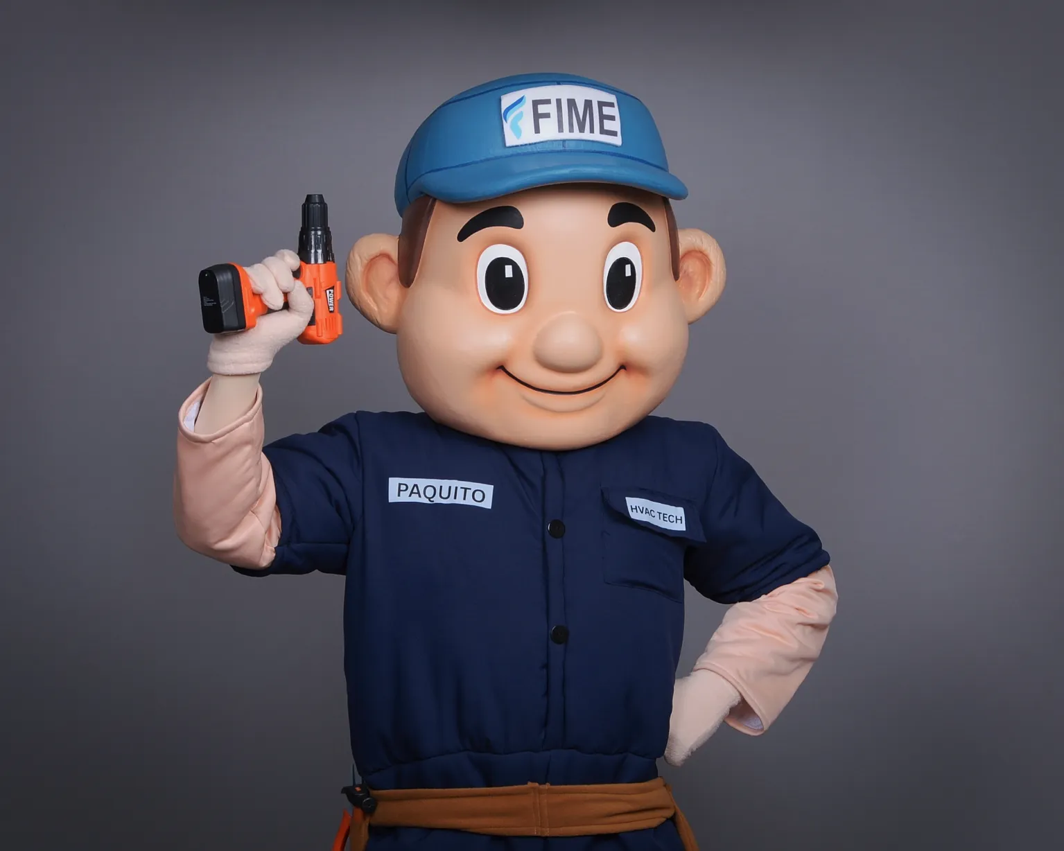 Mascot in blue uniform and cap holding an orange drill, smiling with one hand on hip, gray background.