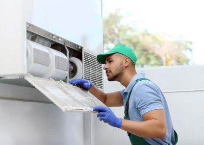 Man in uniform and gloves cleaning an air conditioner filter indoors.