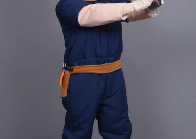 Person in a cartoon handyman costume holding a toy drill, standing on a wood floor with a gray background.